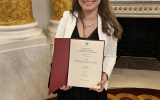 studentka stoi w sali balowej zamku królewskiego trzymając w rękach dyplom.