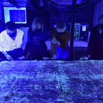 We wnętrzu pracownie cztery postacie oglądają obraz w świetle ultrafioletowym