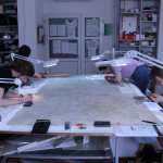 cztery studentki pracują nad konserwacją obrazu. Do stołu przypięte są podświetlane lupy