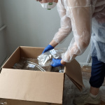 kobieta w stroju ochronnym pakuje fragmenty zabytkowej tkaniny do pudełka